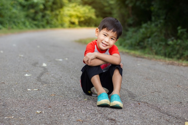 Młody azjatykci śliczny chłopiec obsiadanie i patrzeć na drodze w parku