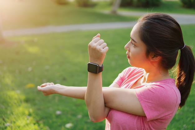 Zdjęcie młody azjatykci sprawności fizycznej kobiety odzieży smartwatch rozciągania ręki przed ćwiczeniem w parku ,.