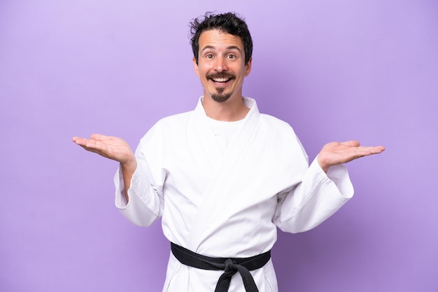Młody biały mężczyzna robi karate izolowany na fioletowym tle z zszokowanym wyrazem twarzy