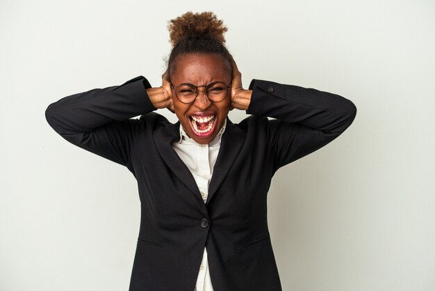 Młody biznes african american kobieta na białym tle obejmujące uszy rękami starając się nie słyszeć zbyt głośnego dźwięku.