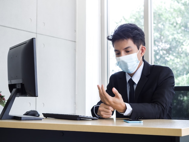 Młody biznesmen azjatyckich w garniturze noszenie maski medyczne coraz ból dłoni podczas korzystania z komputera przenośnego w biurze
