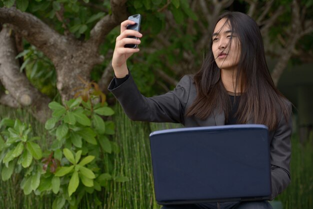 Młody biznesmen azjatyckich z długimi włosami przy selfie w parku
