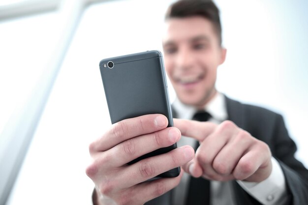 Młody biznesmen czyta SMS-a w telefonie siedząc w biurze
