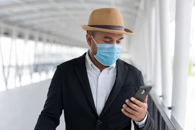 Młody biznesmen noszenie maski ochronnej i za pomocą smartfona
