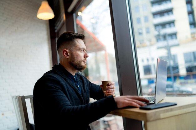 Młody biznesmen pracy z laptopem na odległość. Przystojny mądry mężczyzna ma pracę w kawiarni.