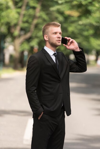 Młody biznesmen rozmawia przez telefon, stojąc na zewnątrz w ParkxA