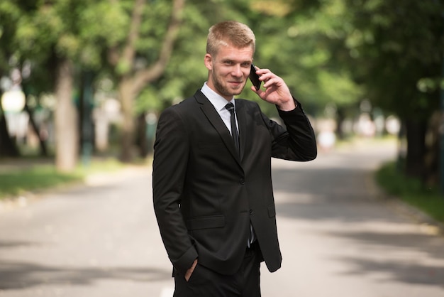 Młody Biznesmen Rozmawia Przez Telefon, Stojąc Na Zewnątrz W Parkxa