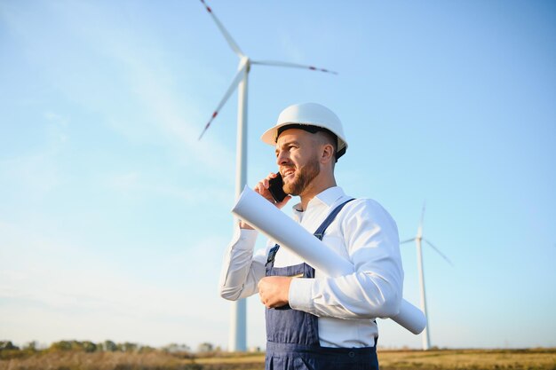 Młody biznesmen rozmawia z menedżerem za pomocą inteligentnego telefonu na polu turbiny wiatrowej, koncepcja zielonej energii