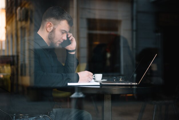 Młody Biznesmen Rozmawia Z Telefonu Komórkowego Podczas Pracy Na Laptopie W Kawiarni