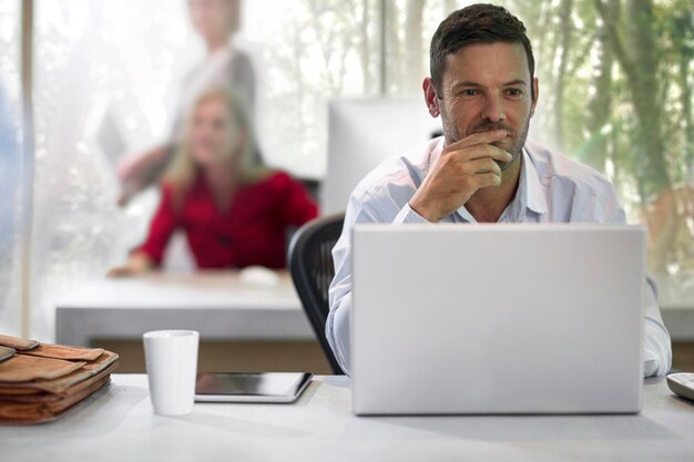 Młody biznesmen siedzący w biurze, używający laptopa