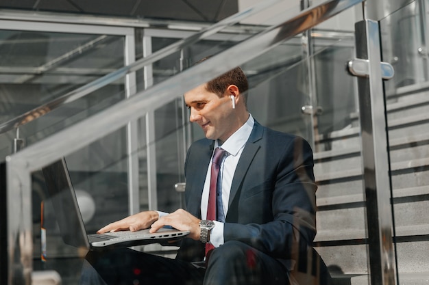 Młody biznesmen siedzi na schodach i pracuje na laptopie. Młody mężczyzna siedzi na schodach i pracuje na laptopie.