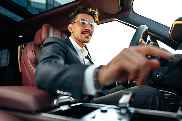 Młody biznesmen w eleganckim garniturze prowadzący luksusowy samochód
