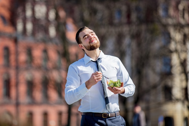 Młody biznesmen w koszuli i krawacie z sałatką pudełko na lunch