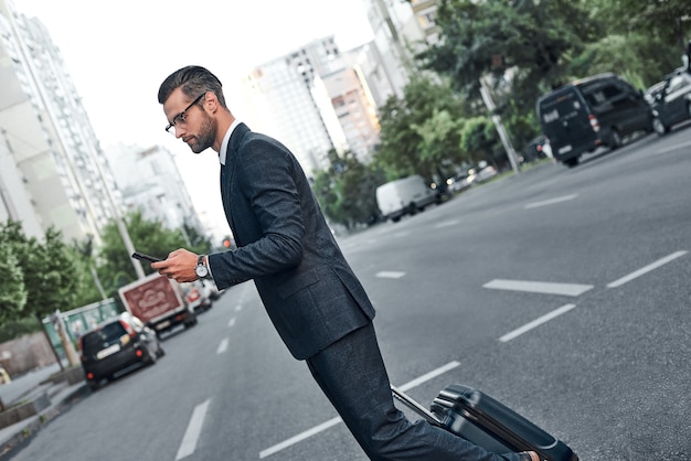 Zdjęcie młody biznesmen w okularach rozmawia na swoim smartfonie i przechodzi przez ulicę