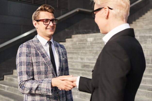 Młody biznesmen w okularach, ściskając ręce do interesu stojącego na schodach na zewnątrz