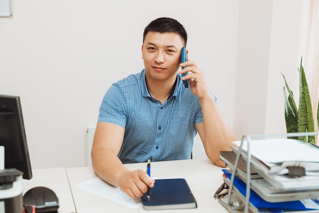 Młody biznesmen z Azji rozmawia przez telefon o pracy w biurze, mężczyzna jest Azjatą