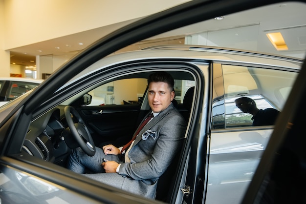 Młody Biznesmen Ze Sprzedawcą Patrzy Na Nowy Samochód W Salonie Samochodowym. Kupowanie Samochodu.