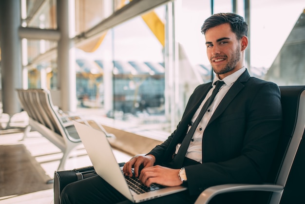 Młody biznesowego mężczyzna obsiadanie na komputerze z walizką przy lotniskiem czeka lot