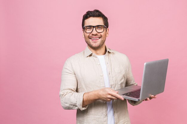 Młody Biznesowy Mężczyzna Jest Ubranym Szkła Pracuje Używać Komputerowego Laptop Z Uśmiechem Odizolowywającym Nad Menchii ścianą.