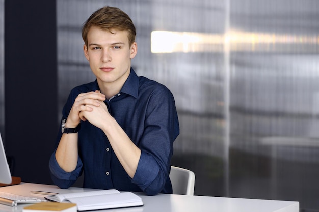 Młody blond biznesmen myślący o strategii w swoim miejscu pracy z komputerem.