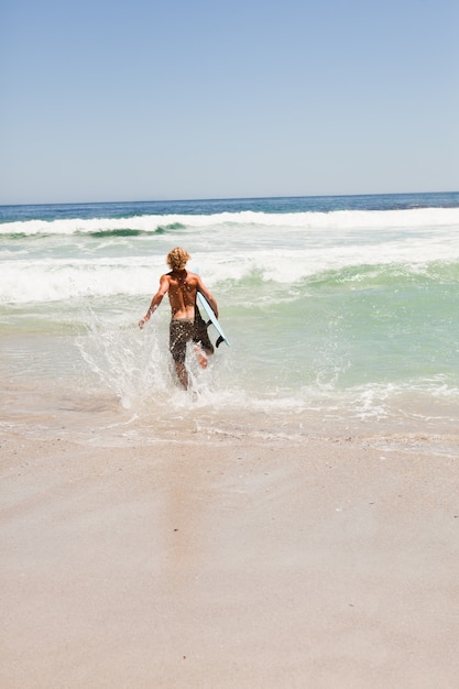 Młody blondynka mężczyzna bieg w wodzie z jego surfboard