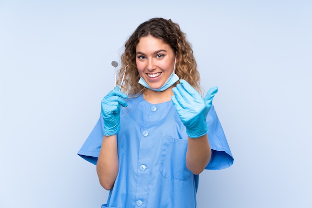 Młody blondynki kobiety dentysty mienia narzędzia na błękit ścianie zaprasza przychodzić