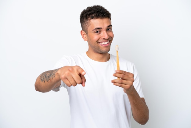 Młody Brazylijczyk szczotkujący zęby na białym tle wskazuje palcem na ciebie z pewną siebie miną
