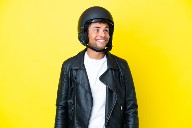 Młody Brazylijczyk w kasku motocyklowym na żółtym tle myślący o pomyśle, patrząc w górę