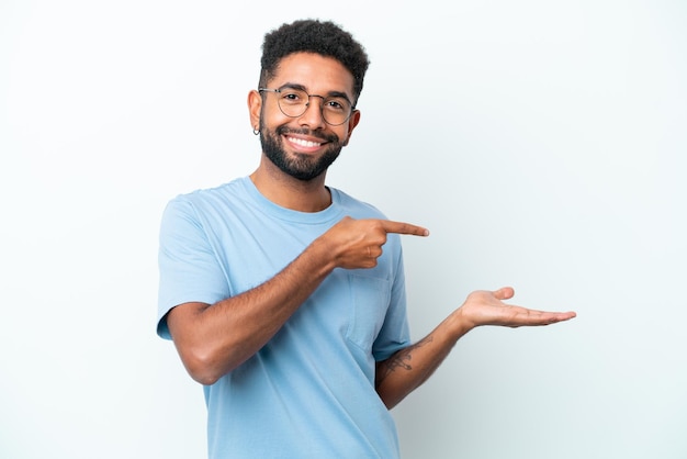 Młody brazylijski mężczyzna na białym tle trzymając copyspace wyimaginowany na dłoni, aby wstawić reklamę