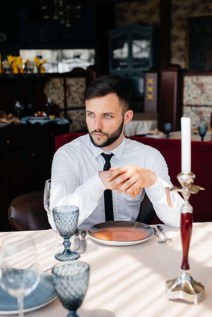 Młody, brodaty biznesmen siedzi przy stoliku w eleganckiej restauracji i czeka na swoje zamówienie. Obsługa klienta w cateringu.