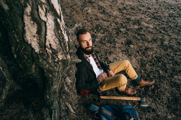 Młody brodaty hipster mężczyzna relaksujący siedzący pod drzewem w lesie Koncepcja podróży