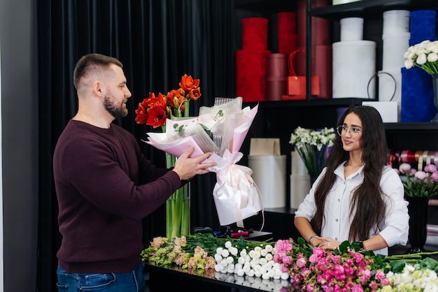 Młody brodaty mężczyzna kupuje piękny bukiet kwiatów na dziewczęce wakacje w przytulnej kwiaciarni Kwiaciarnia i robienie bukietów w kwiaciarni Mały biznes