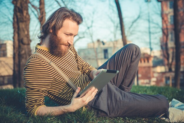 młody brodaty stylowy przystojny mężczyzna hipster za pomocą tabletu