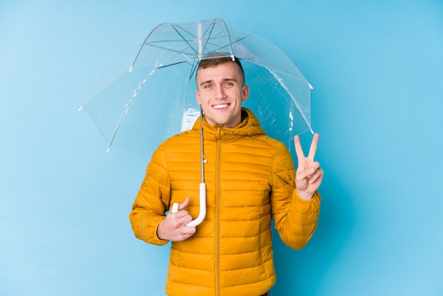 Zdjęcie młody caucasian mężczyzna trzyma parasol pokazuje numer dwa z palcami.