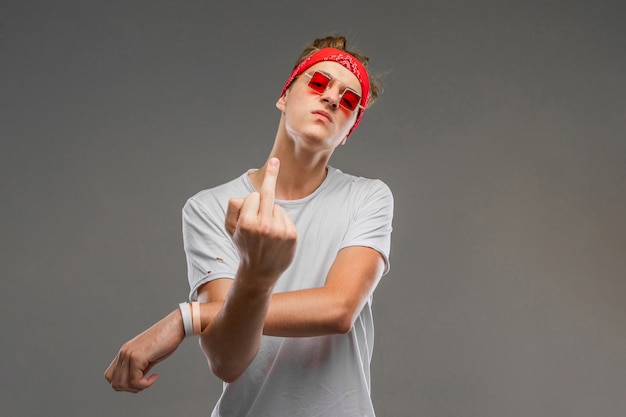 Młody caucasian mężczyzna w czerwonych okularach przeciwsłonecznych, biała koszulka pozuje na szarości ścianie