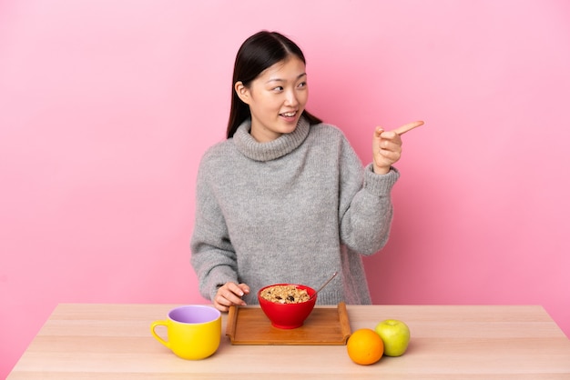 Młody chiński dziewczyna o śniadanie w tabeli wskazując palcem w bok i prezentuje produkt