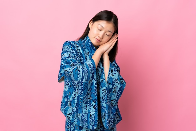 Młody chiński dziewczyna ubrana w kimono na białym tle dokonywanie gestu snu w dorable wypowiedzi