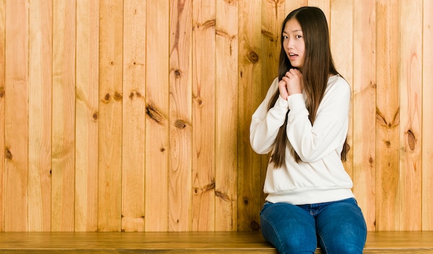 Młody chiński kobieta siedzi na drewnianym miejscu przestraszonym i przestraszonym.