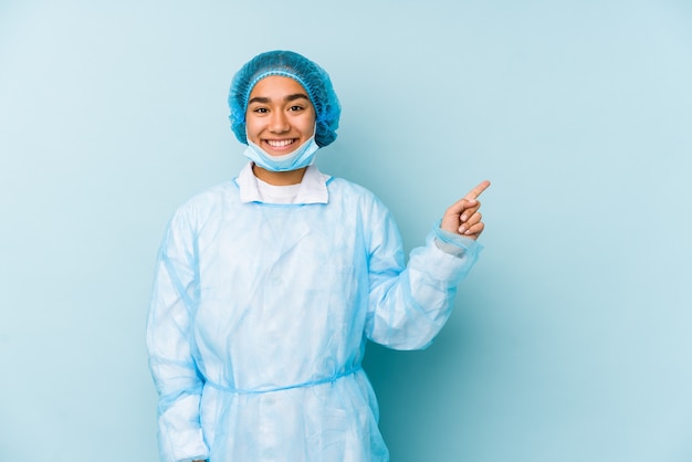 Młody chirurg azjatycka kobieta na białym tle, uśmiechając się i wskazując na bok, pokazując coś w pustej przestrzeni.