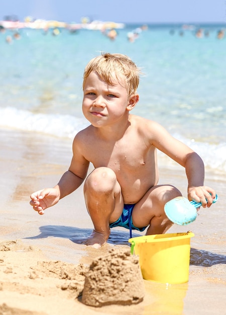 Młody chłopak bawi się w piasku i falach na plaży