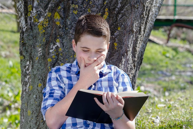 Młody chłopak czytający książkę w lesie z małą głębią ostrości i przestrzenią do kopiowania