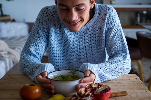 Zdjęcie młody chłopak nastolatek uśmiech patrząc zupa warzywna w domu w porze lunchu - wegetariańska i zdrowa żywność odżywianie koncepcja styl życia - chłopiec ludzie i kolory jesieni kryty