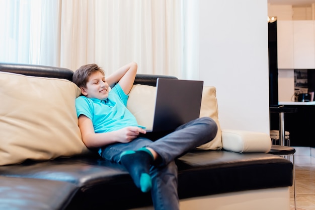 Młody chłopak ogląda zabawne filmy w domu podczas kwarantanny. nastolatka siedząca na wygodnej kanapie w domu,