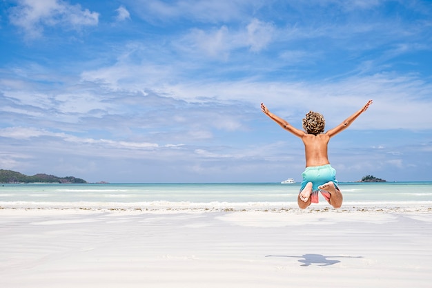 Młody chłopak skacze z radości i zabawy na tropikalnej plaży, koncepcja wakacji letnich