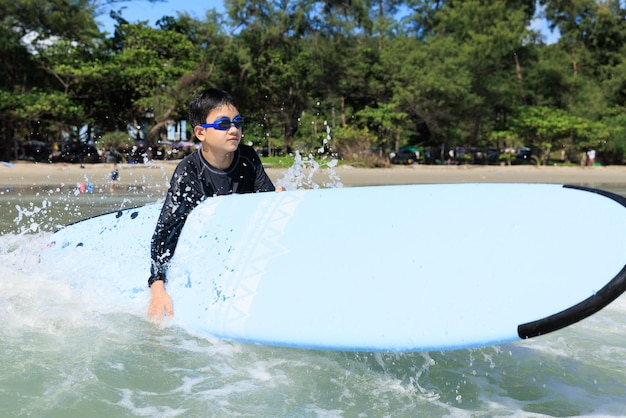Zdjęcie młody chłopak student w surfingu, trzymając deskę miękką i próbując przywrócić ją do brodzenia w morzu, aby ćwiczyć podczas gry przeciwko falom i rozpryskiwaniu wody