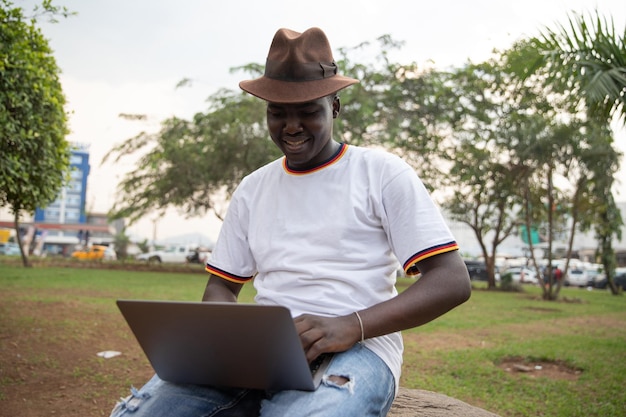 Młody chłopak z Afryki korzysta z laptopa w parku na świeżym powietrzu Młodzi ludzie i technologia w Afryce