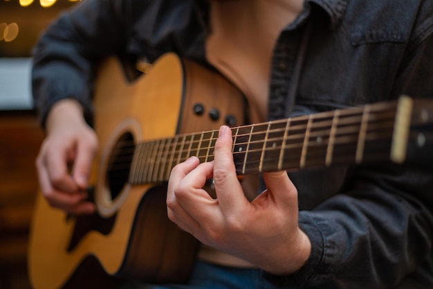 Młody chłopak z brodą gra na gitarze akustycznej w pomieszczeniu z ciepłym oświetleniem