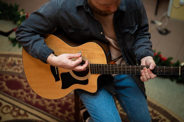 Młody chłopak z brodą gra na gitarze akustycznej w pomieszczeniu z ciepłym oświetleniem