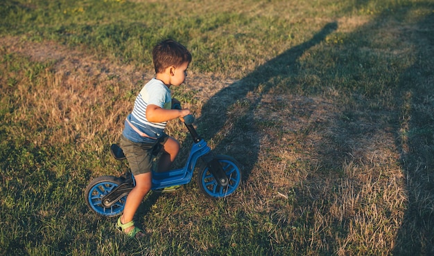 Młody chłopiec kaukaski jedzie na rowerze na zielonym polu radość w słoneczny letni wieczór