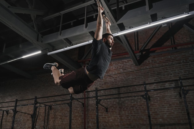 Młody crossfit sportowiec huśta się na kółkach gimnastycznych, robi podciąganie na siłowni Ćwiczenia treningowe